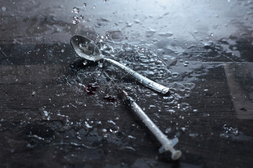 a teaspoon and a syringe with a drug in the rain on a gray surface, near a drop of blood