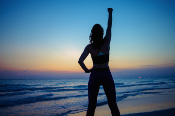 Fototapeta premium woman with raised arms rejoicing on ocean shore in evening