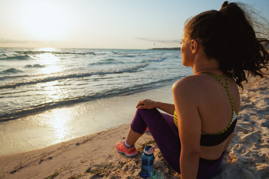 woman with water sitting and relaxing on seashore in evening