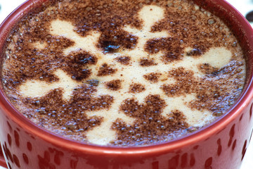 A foamy mug of cappuccino coffee with chocolate snowflake motif and a snowy background with a scattering of coffee beans sets the scene for a festive Christmas and warming up in cold winter weather