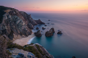 Sunset over a hidden surreal Praia Da Ursa Beach. Cabo Da Roca with light-house in background. Atlantic coast, Portugal, Europe