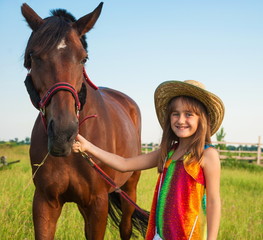 Little girl in cowboy hat holds  horse under  bridle