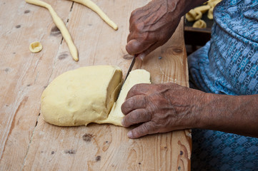 Cut the dough for the homemade orecchiette baresi. Working hands. Hands of an elderly woman. Italian owners of small business. Typical fresh pasta from Bari, Puglia region, Italy. Ancient tradition.