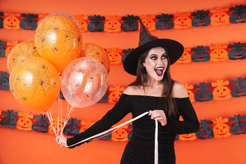 Image of amazed witch girl in black halloween costume holding balloons