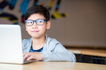 Smart looking Asian preteen boy with eye blue light blocking glasses rolling eyes smiling happily, using computer laptop to study online lessons. Online learning and self study concept.  © myboys.me