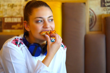 Image of happy woman while sitting in cafe and listening music and eating pizza