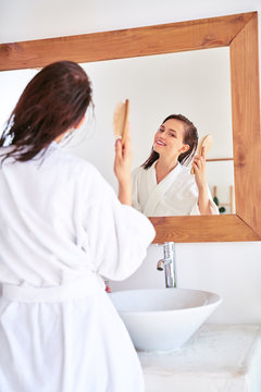 Image of brunette combing her hair in front of bathroom mirror
