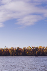 Autumn colorful foliage. Beautiful landscape with lake and colorful trees in fall season. Blue sky with white clouds. Autumn scene of a lake and a forest.