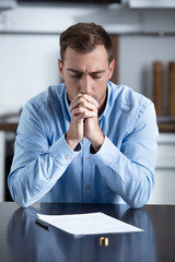 sad man in shirt sitting at table with ring and divorce documents