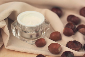 Closeup of a moisturiser in a glass jar surrounded by chestnuts and acorns. Concept of fall skincare.