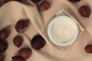Flat lay with a moisturiser in a glass jar surrounded by chestnuts and acorns. Concept of fall skincare.