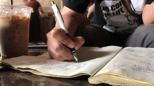 Close up a student writing on a notebook in coffee shop.