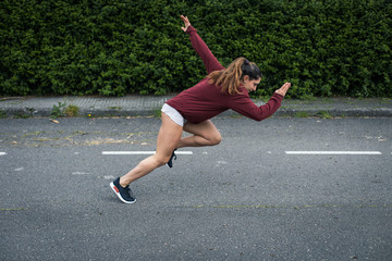 Fast powerful young woman sprinting. Running training on asphalt.
