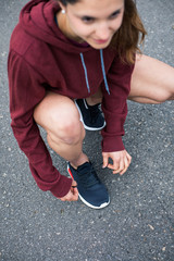 Detail of female athlete lacing running shoes and gettting ready for training on asphalt road.