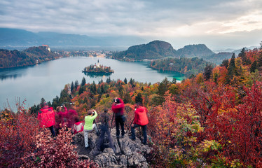 Group of photographers takes picture of Bled lake. Gloomy morning scene in Triglav National Park. Colorful autyumn scene of Julian Alps, Slovemnia, Europe. Traveling concept background.