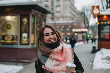 Happy young woman in warm clothing walking on city street during winter
