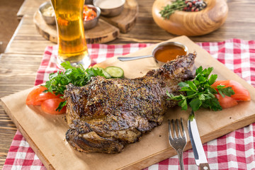 roasted lamb leg with fresh vegetables on wooden board and glass of beer on wooden table