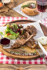 Grilled lamb ribs with green mix and honey sauce on wooden board and glass of red wine on wooden table