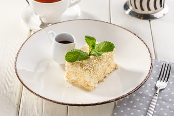 Cake Napoleon puff pastry dessert with cream and cup of black tea on white wooden table