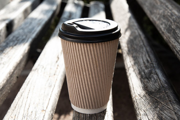 A paper coffee cup with cap on a bench