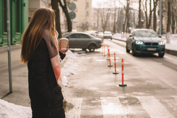  Woman with disposable cup in warm clothing standing in city street in winter