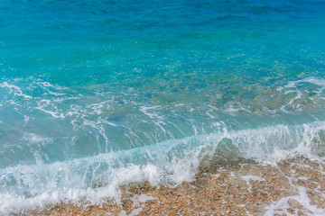 Turquoise sea waves splashing on pebble shore