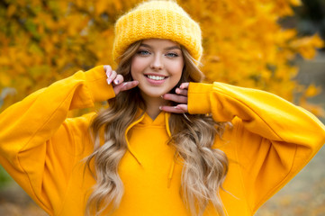 Beautiful girl walking outdoors in autumn. Smiling girl collects yellow leaves in autumn. Young woman enjoying autumn weather.