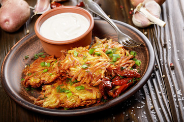 Homemade tasty potato pancakes in clay dish with sun-dried tomatoes and sour cream