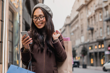 Young asian woman texting while enjoying a day shopping - obrazy, fototapety, plakaty