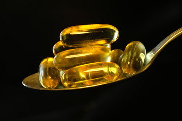 Close up shot Fish oil capsules with omega 3 and vitamin D on stainless steel spoon, healthy diet concept.