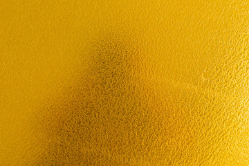 Uneven surface with grit texture of golden colour, shadow of photographer