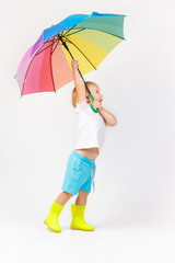 A handsome boy in yellow boots holds a colorful bright umbrella blown away by the wind. Idea for advertising a store of children's clothing and accessories.