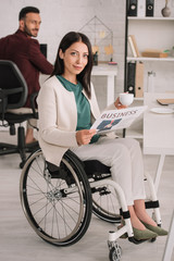 smiling disabled businesswoman looking at camera while holding coffee cup and newspaper