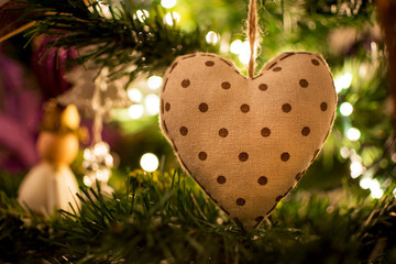 Closeup view of a Christmas tree ball with a heart shape and lights from inside the tree