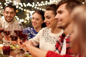 holidays and celebration concept - happy friends having christmas dinner at home, drinking red wine and clinking glasses