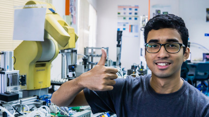 A young Malay engineering student with spectacles working in the lab and show a thumbs up sign.