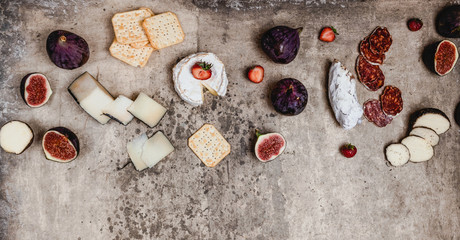 assortment of cheese with figs, grapes, ham and crackers on shabby background, top view