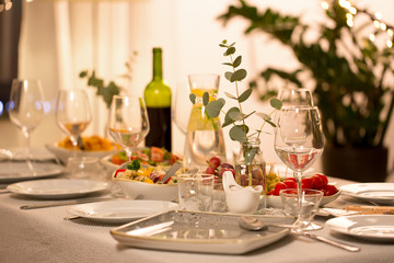 celebration, holidays, catering and eating concept - eucalyptus branch on table served with plates, wine glasses and food for home dinner party