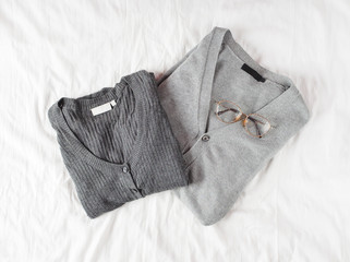 Grey sweaters and stylish glasses laying on white linen background. Flat lay. Top view