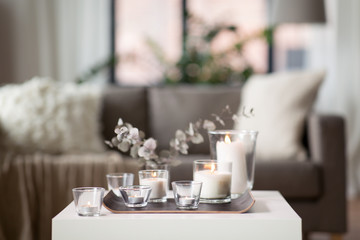 decoration, hygge and cosiness concept - burning white fragrance candles on tray and branches of eucalyptus populus on table at cozy home