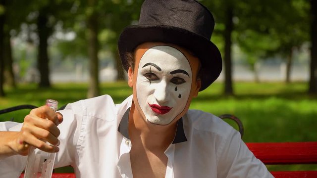 Close-up of a mime drinks alcohol outdoors. Bad habits