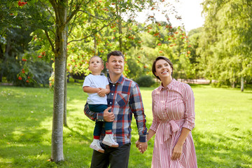 family, leisure and people concept - happy mother, father and little son looking up at summer park