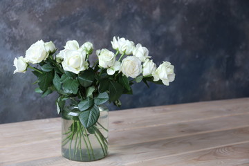 a bouquet of white roses in a glass vase in a room with a concrete gray wall