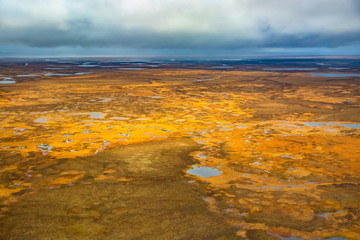 Fototapeta na wymiar Photographing from a helicopter in the Arctic. Autumn nature landscape of the northern tundra. The landscape of many lakes, rivers, variegated mosses and lichens. Gloomy autumn sky.