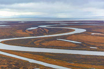 Photographing from a helicopter in the Arctic. Autumn nature landscape of the northern tundra. The landscape of many lakes, rivers, variegated mosses and lichens. In the background the coast of the Ar