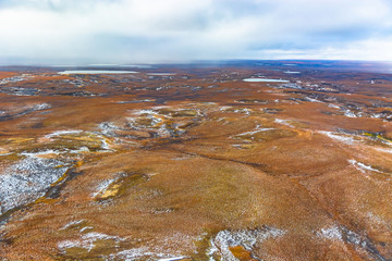 Photographing from a helicopter in the Arctic. Autumn nature landscape of the northern tundra. The landscape of many lakes, rivers, variegated mosses and lichens. The first snow fell in the folds of t