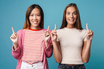 Portrait of multinational delighted women pointing fingers upward