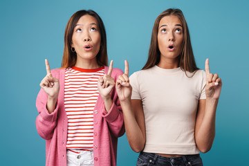 Portrait of multinational shocked women pointing fingers upward