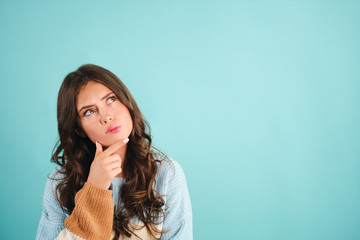 Fototapeta premium Attractive thoughtful girl in sweater dreaming over blue background