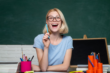 Portrait of a female student in university. Student and tutoring education concept. Funny female young teacher in the classroom. Young teacher in glasses over green chalkboard background.
